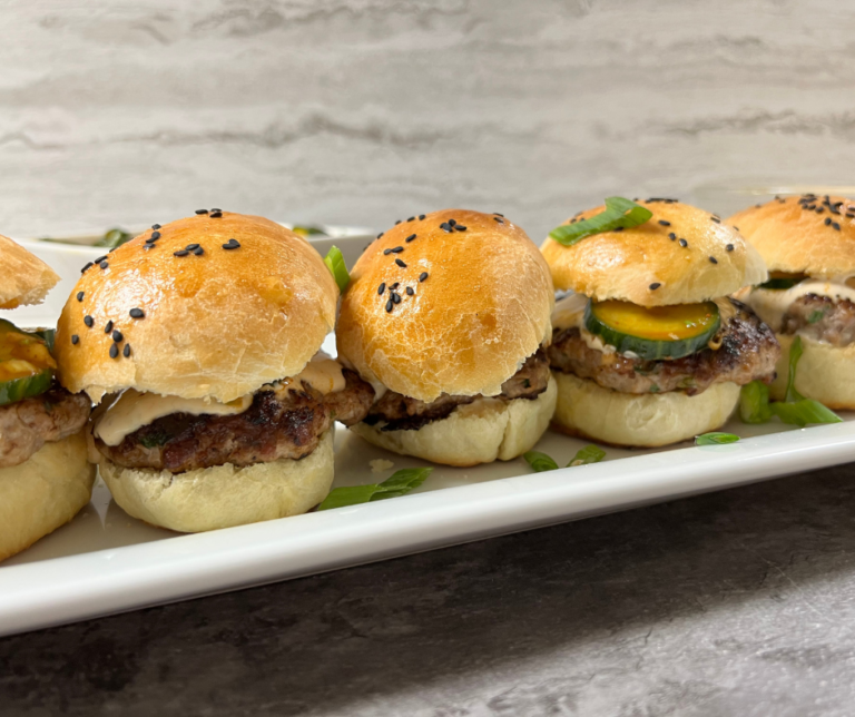 Close up image of Pork Wonton Burgers in a line on a platter with homemade black sesame seed buns and asian cucumber salad