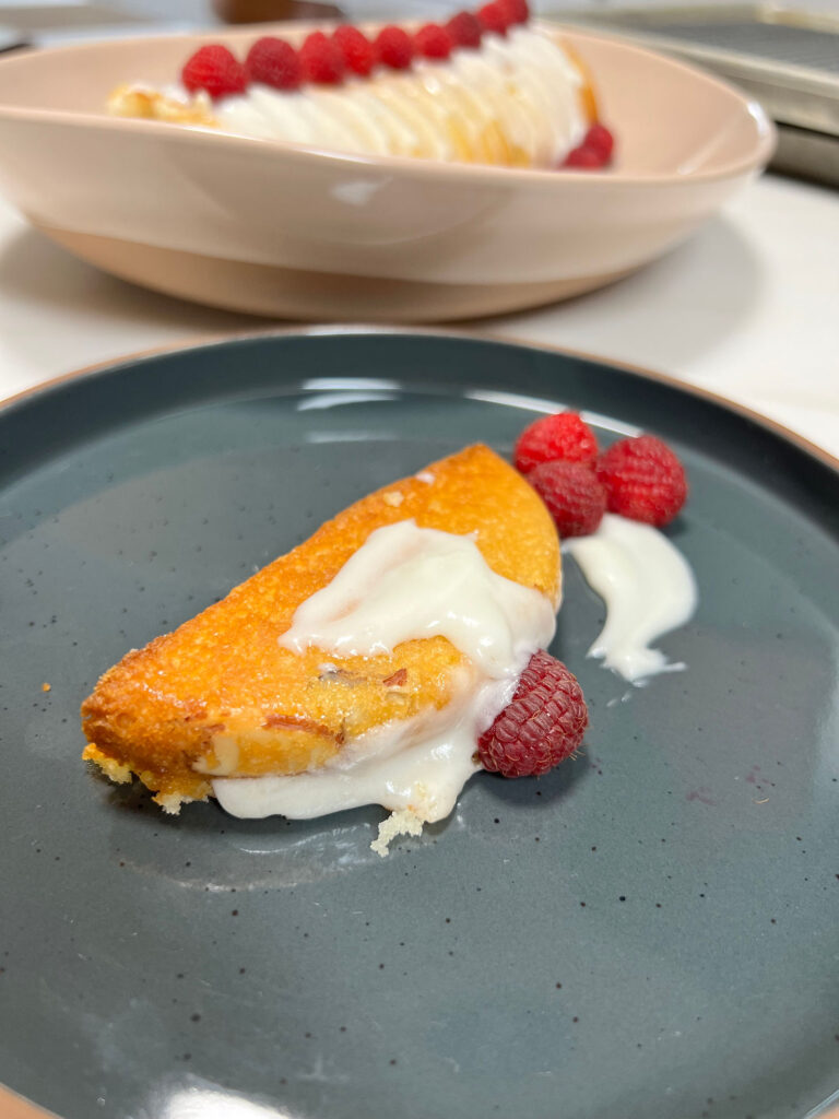 A slice of the Lychee Almond Cake with the frosting and a fresh raspberry