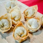 Fried wontons in the circle (or ignot) shape on a bamboo cutting board