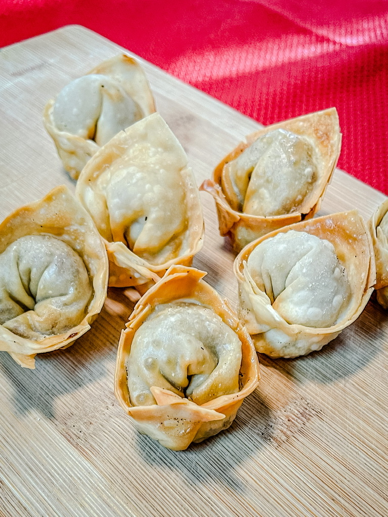 Fried wontons in the circle (or ignot) shape on a bamboo cutting board