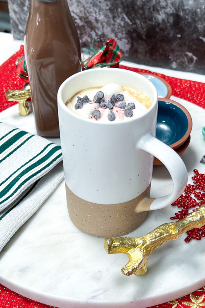 finished coffee, topped with crushed peppermint, mini chocolate chips and whipped cream. The coffee creamer is in a bottle in the background
