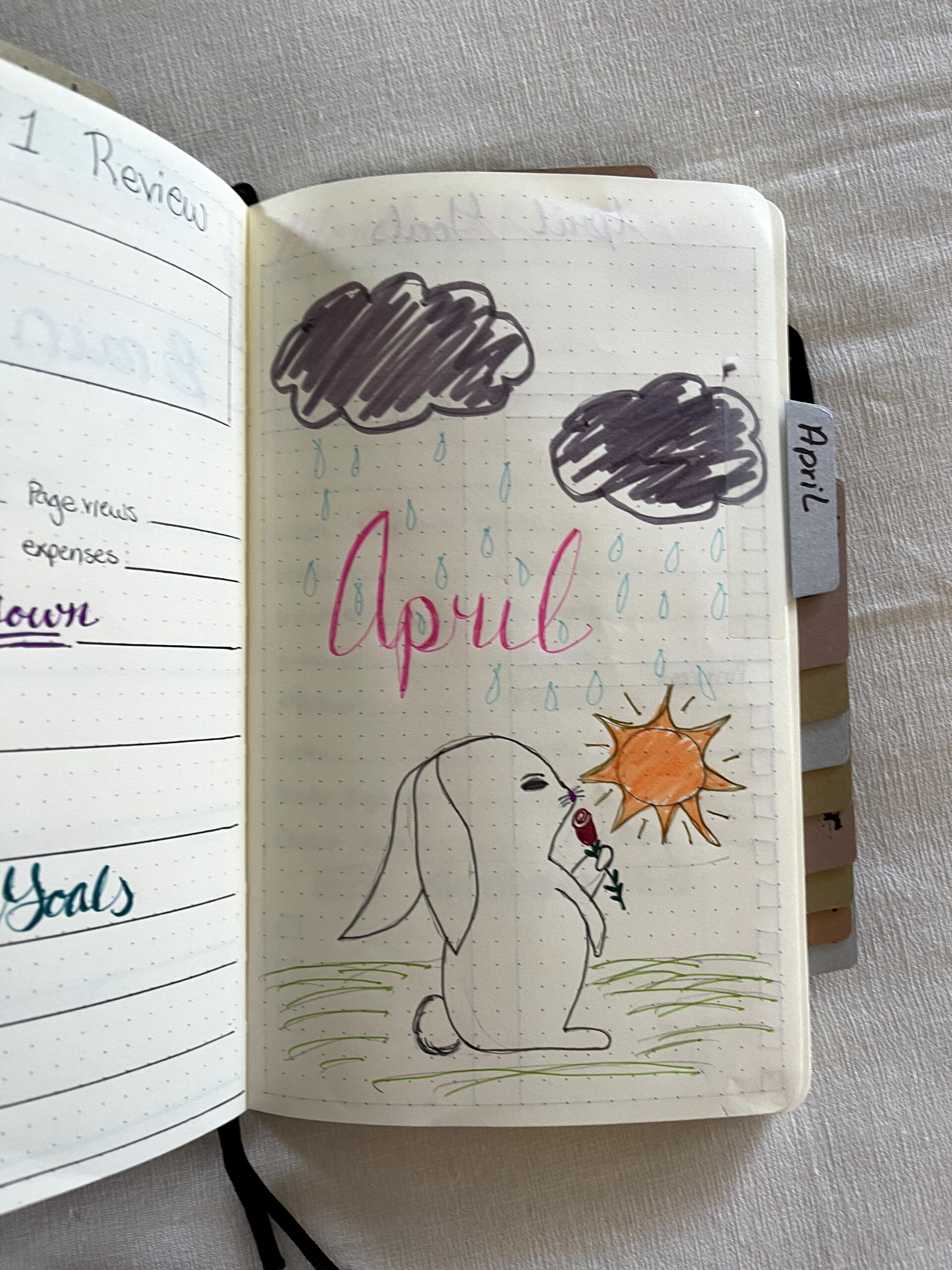 Image of the April Month Cover - a bunny smelling a rose with dark gray clouds and the sun peaking out.