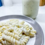 alfredo sauce covering rotini on a ceramic plate next to a jar of the sauce.