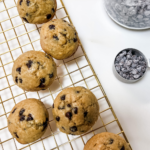 chocolate chip muffins on a cooling rack next to a scoop of mini chocolate chips