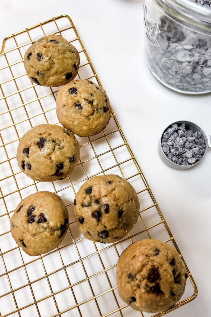 chocolate chip muffins on a cooling rack next to a scoop of mini chocolate chips
