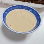 a bowl os Asian Remoulade in front of a tray of hamburgers sitting on top of a white counter
