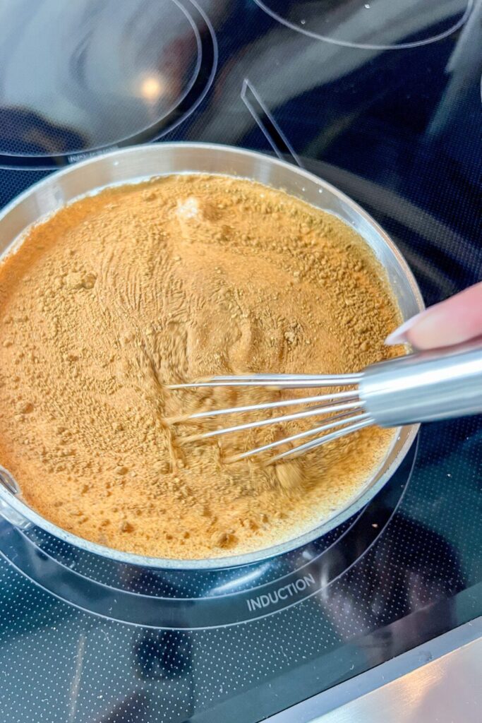 a person using a whisk to stir the Pumpkin Spice Coffee Creamer ingredients in a pot