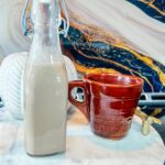 a bottle of Pumpkin Spice Coffee Creamer sits on a marble platter next to a coffee cup with the Pumpkin Spice Coffee Creamer and coffee