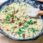 a skillet filled with Smoked Gouda and Bacon Mac and Cheese, topped with parsley on a cutting board