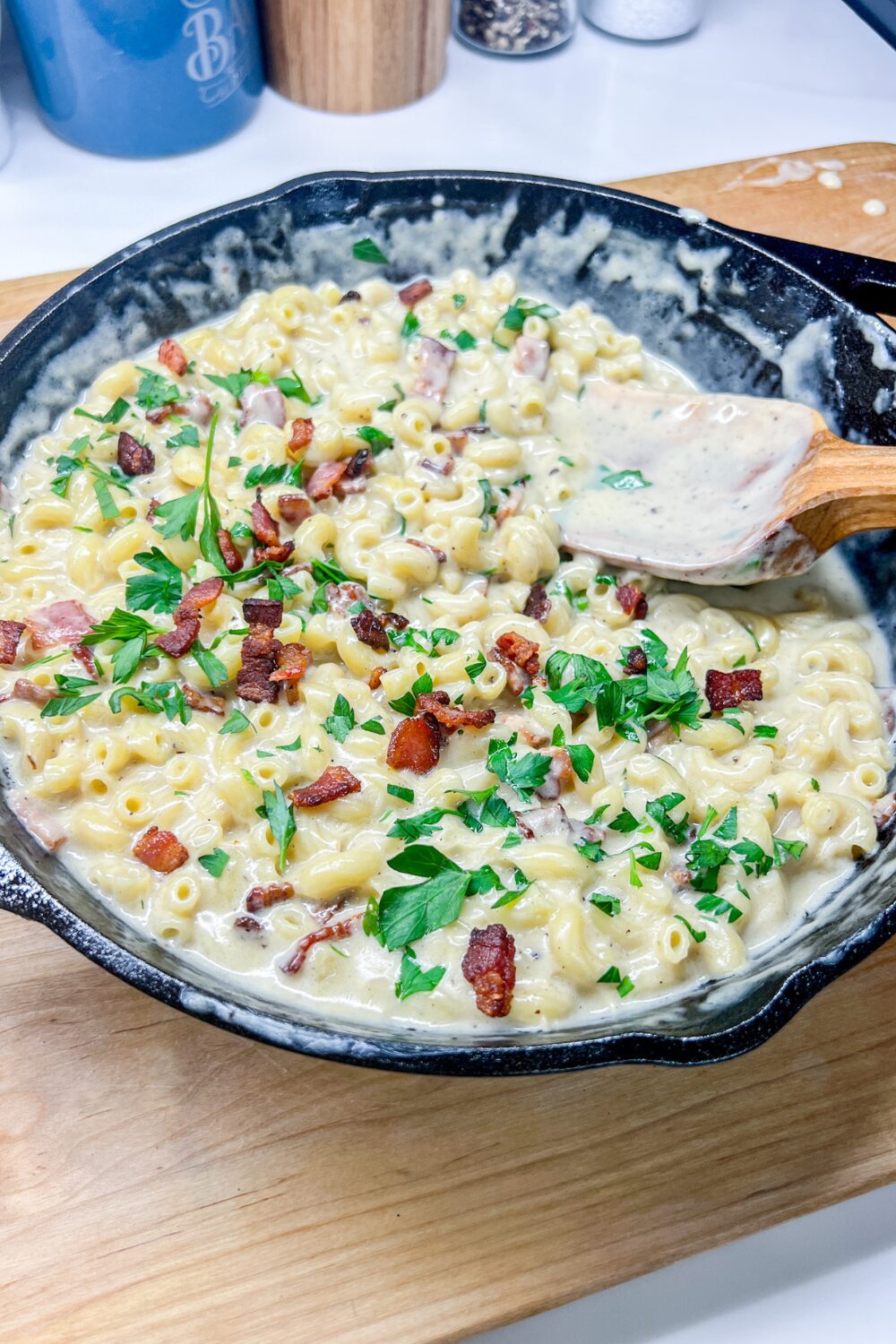 a skillet filled with Smoked Gouda and Bacon Mac and Cheese, topped with parsley on a cutting board