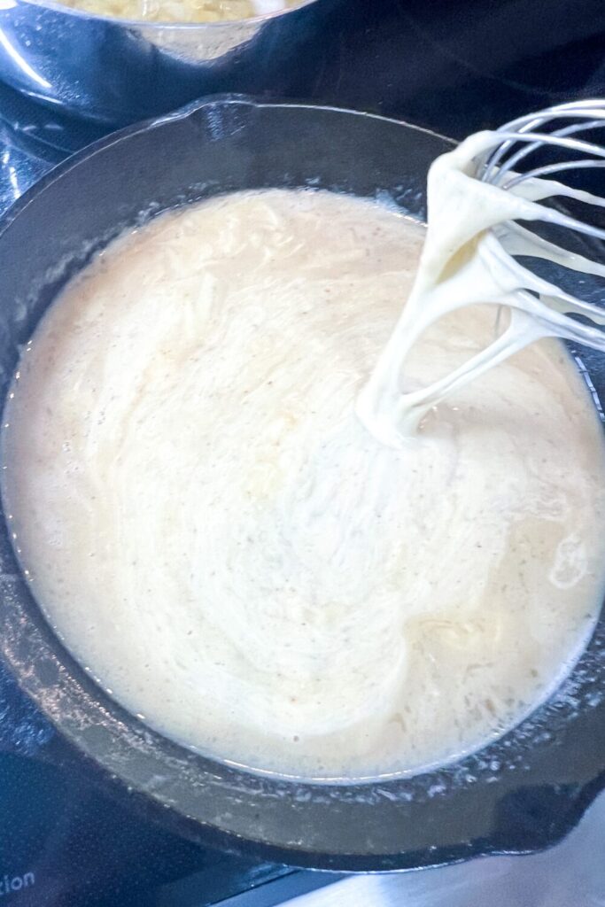 a whisk being used to stir the cheesey mixture in a skillet