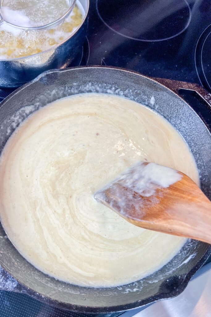using a wood turner to stir around the milk into the cheese sauce.