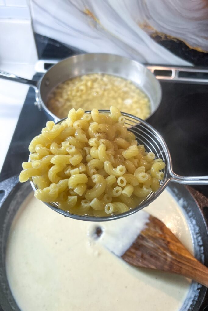 a person holding a ladle full of macaroni over cheese sauce