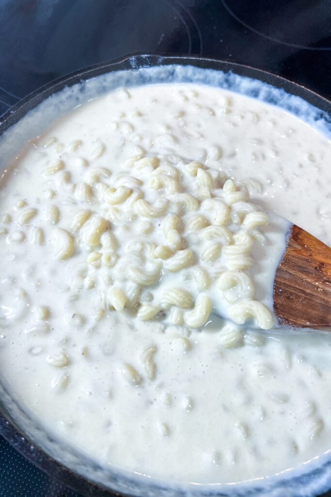 a pan filled with macaroni and cheese being stirred with a wooden spoon