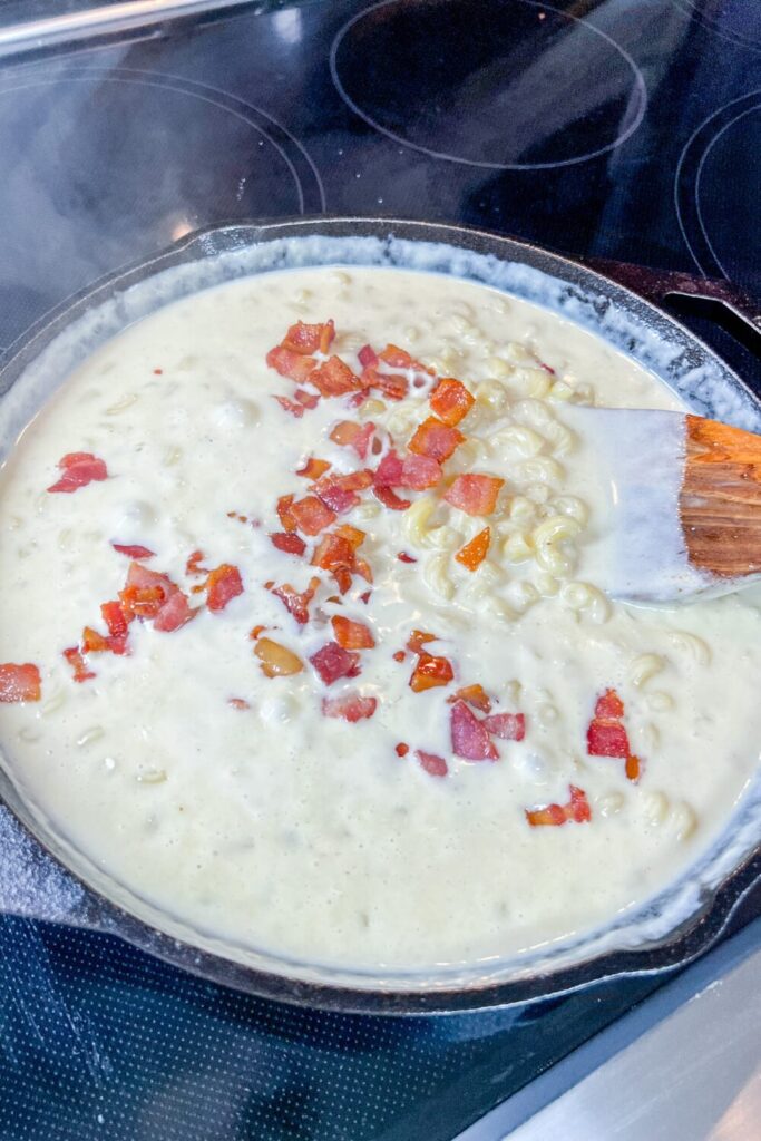 a skillet filled with macaroni and cheese with bacon added on top of a stove