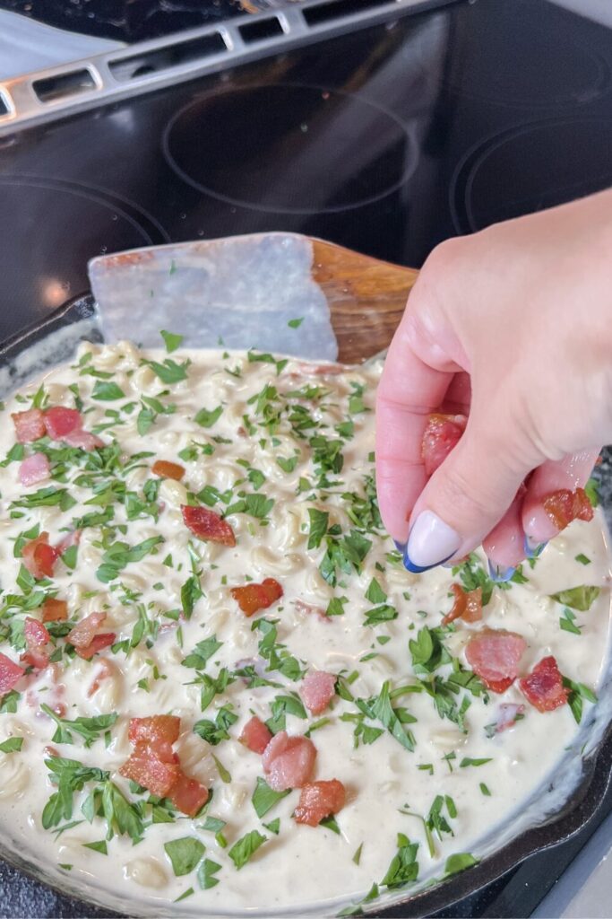 bacon being added to the finished mac and cheese