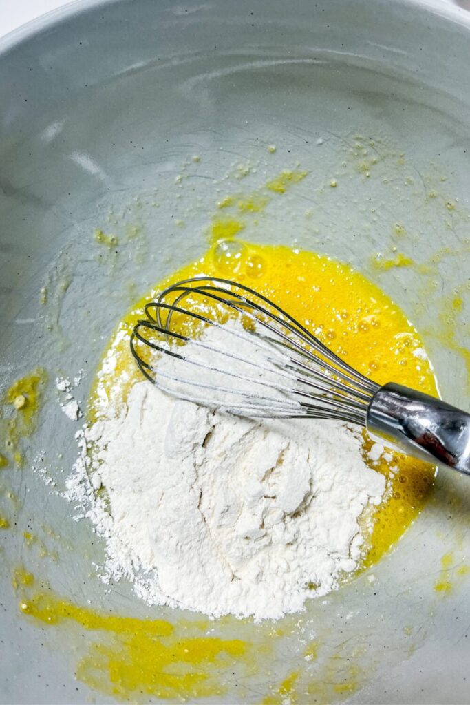 AP and rice flour added to the egg mixture in a bowl with a whisk