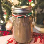 a mason jar filled with hot chocolate mix sits on top of presents under a Christmas tree