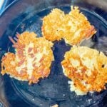 potato pancakes cooking in a skillet on the stove after being flipped (side shown is golden brown)