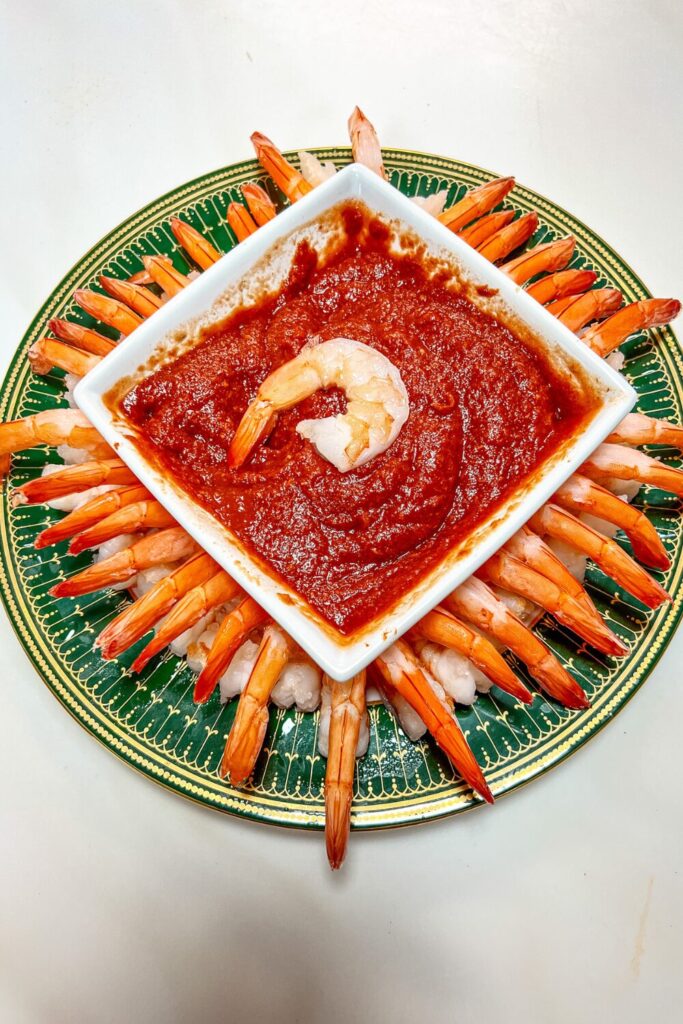 shrimp one a round green and gold plat and a square bowl of sauce in the middle with one shrimp in the middle