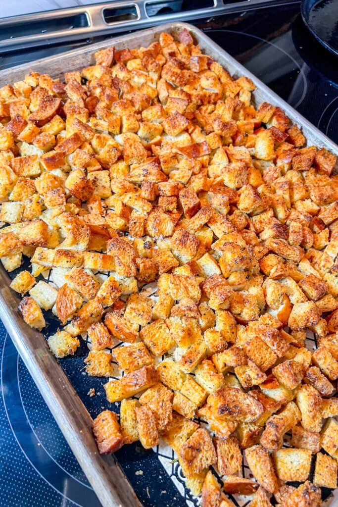 a baking sheet filled with finished croutons sitting on top of an oven