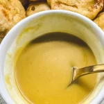 a bowl of honey mustard on a plate of chicken nuggets