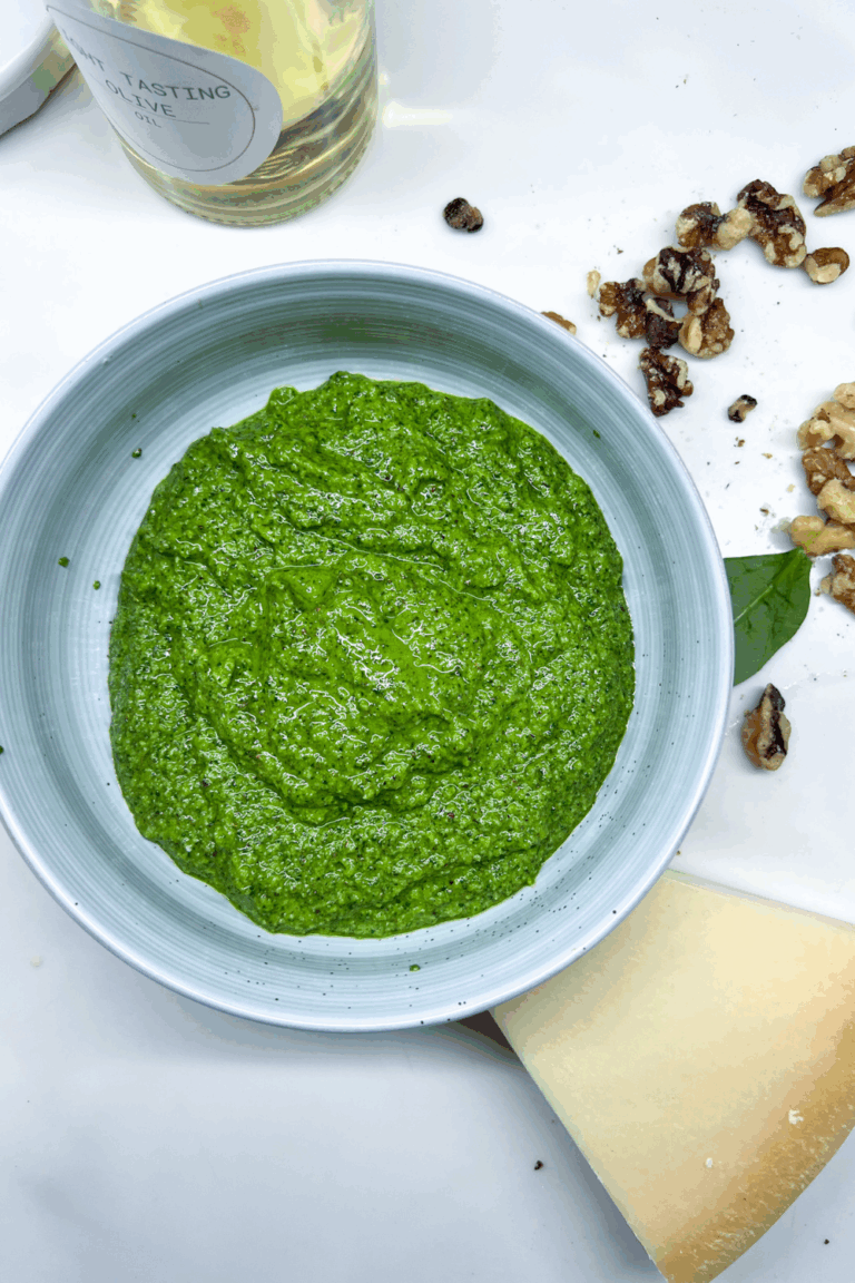 a bowl of finished green pesto next to a bottle of olive oil
