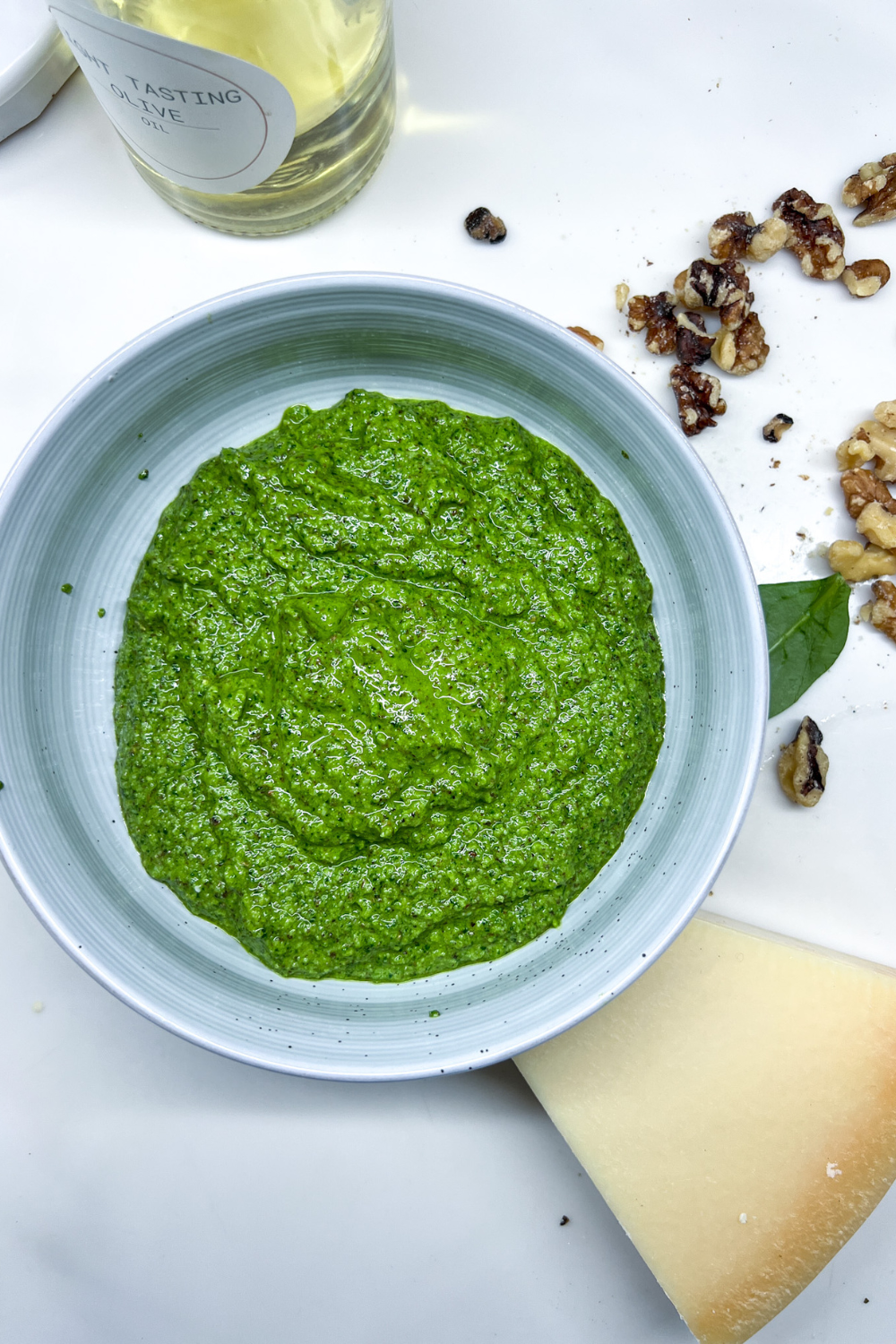 a bowl of finished green pesto next to a bottle of olive oil