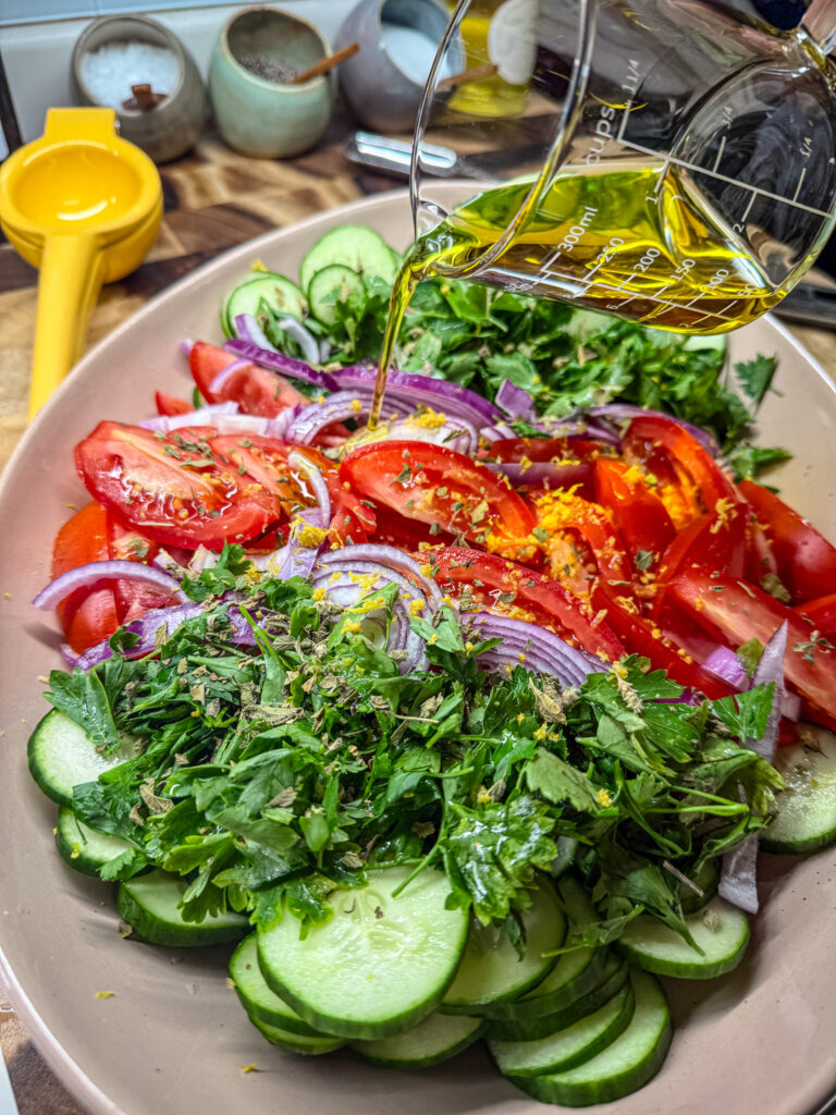 pouring the olive oil over the vegetables for the greek salad