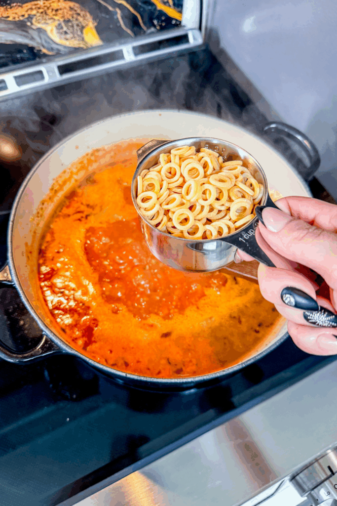 A person holding a measuring spoon over a pot of the Italian Ground Sausage Soup