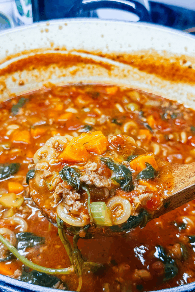 A person holding the Finsihed the Italian Ground Sausage Soup in a ladle over a pot of the soup