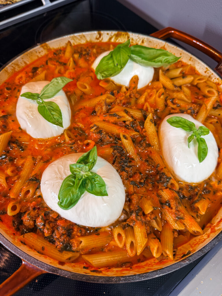 Finished Creamy Arrabbiata Penne with Sausage, topped with burrata and basil leaves.