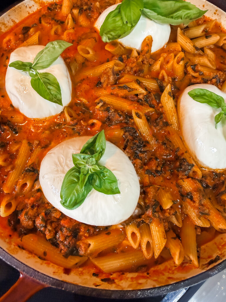 Finished Creamy Arrabbiata Penne with Sausage, topped with burrata and basil leaves.