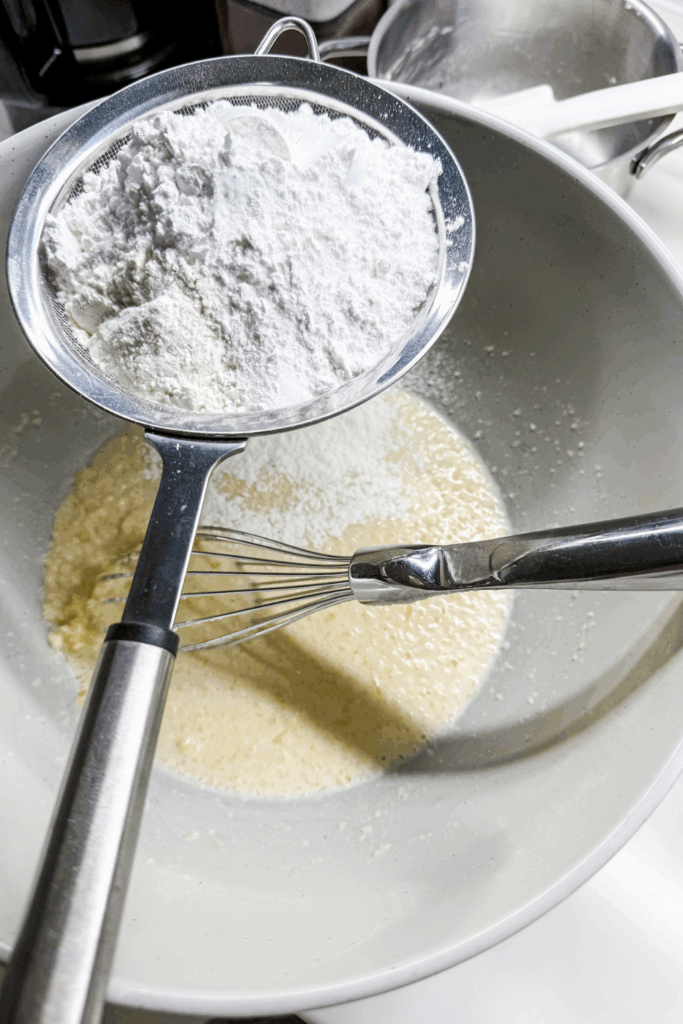 a bowl with the butter-sugar-milk mixture, and the dry ingredients in a sift above the bowl