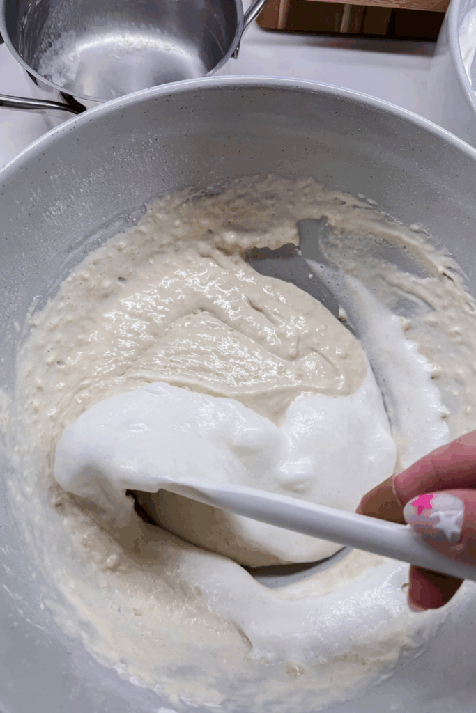 a person using a spatula tofold in the egg whites into the batter in a bowl
