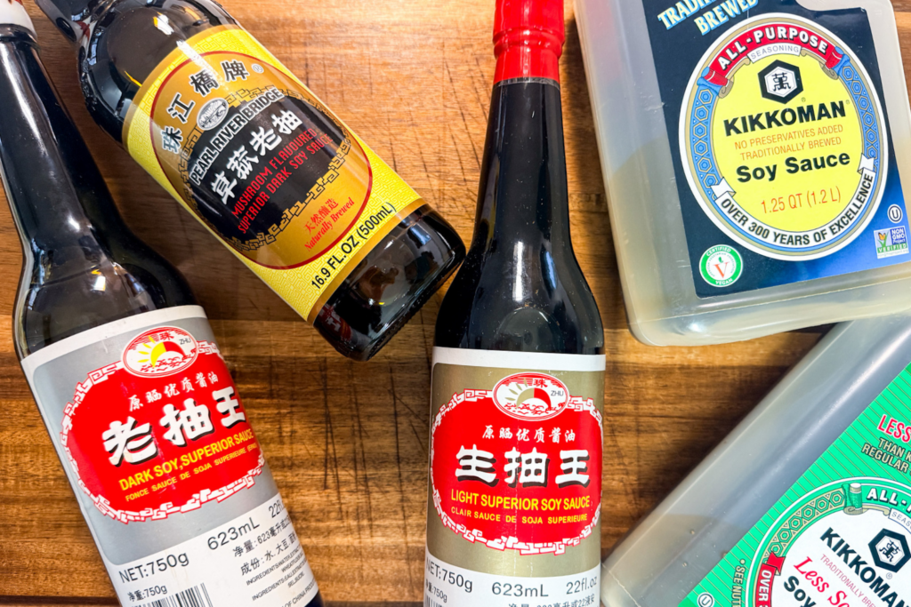 Japanese and Chinese soy sauce bottles including light, dark, mushroom, and low-sodium soy sauce on a wooden cutting board