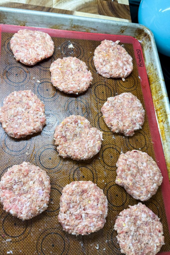 Raw breakfast sausage patties shaped and arranged on a lined sheet pan