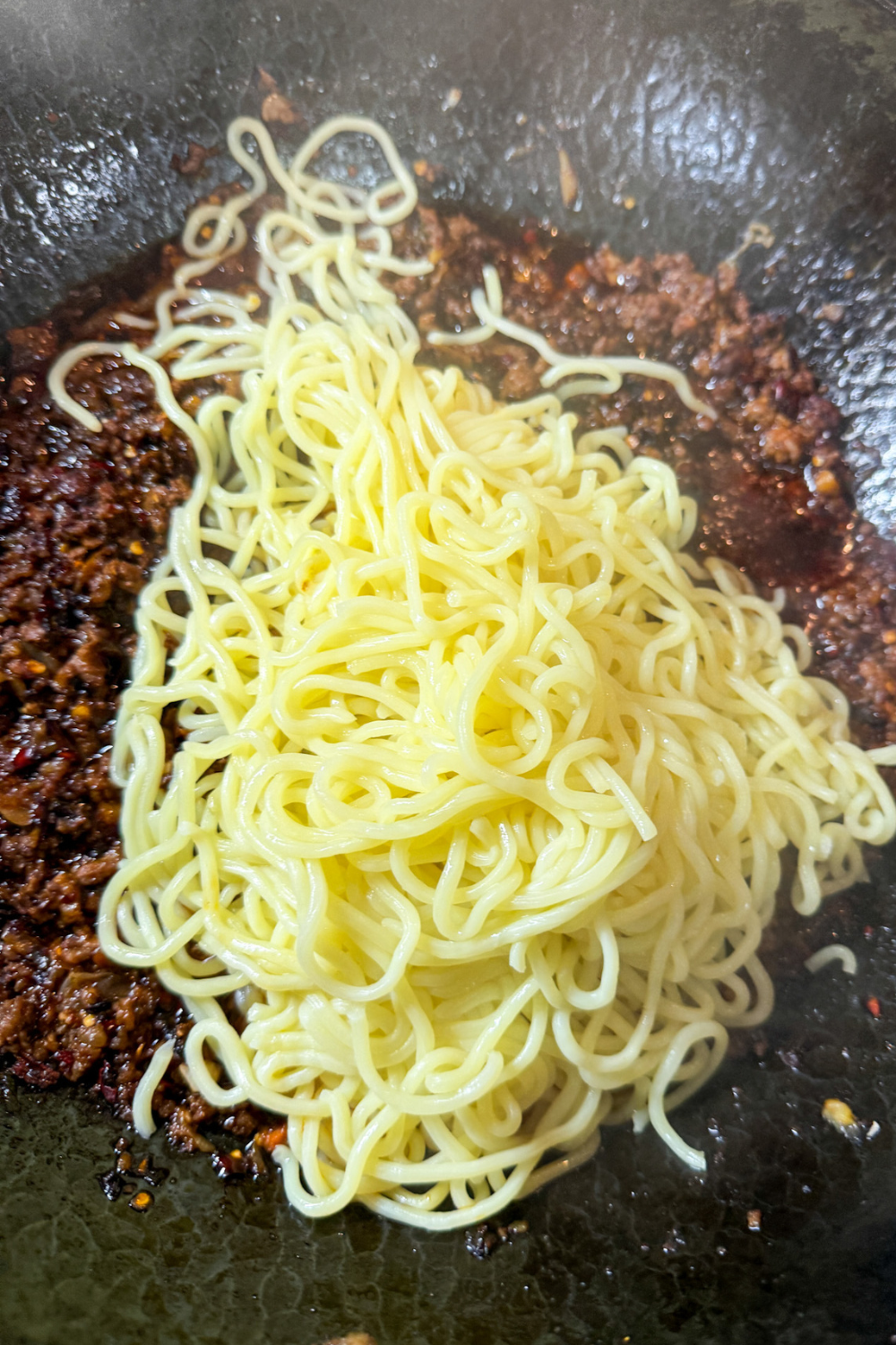 Adding cooked noodles to spicy ground pork sauce for Dan Dan noodles