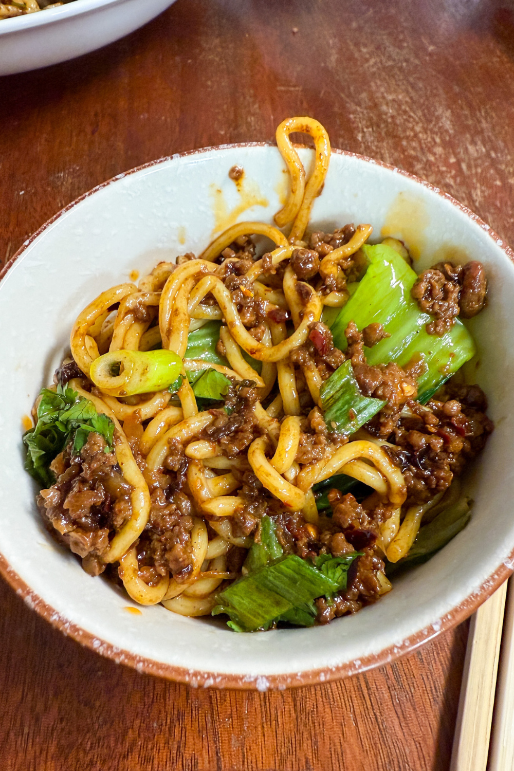 Bowl of homemade Dan Dan noodles with sesame chili sauce, ground pork, and greens