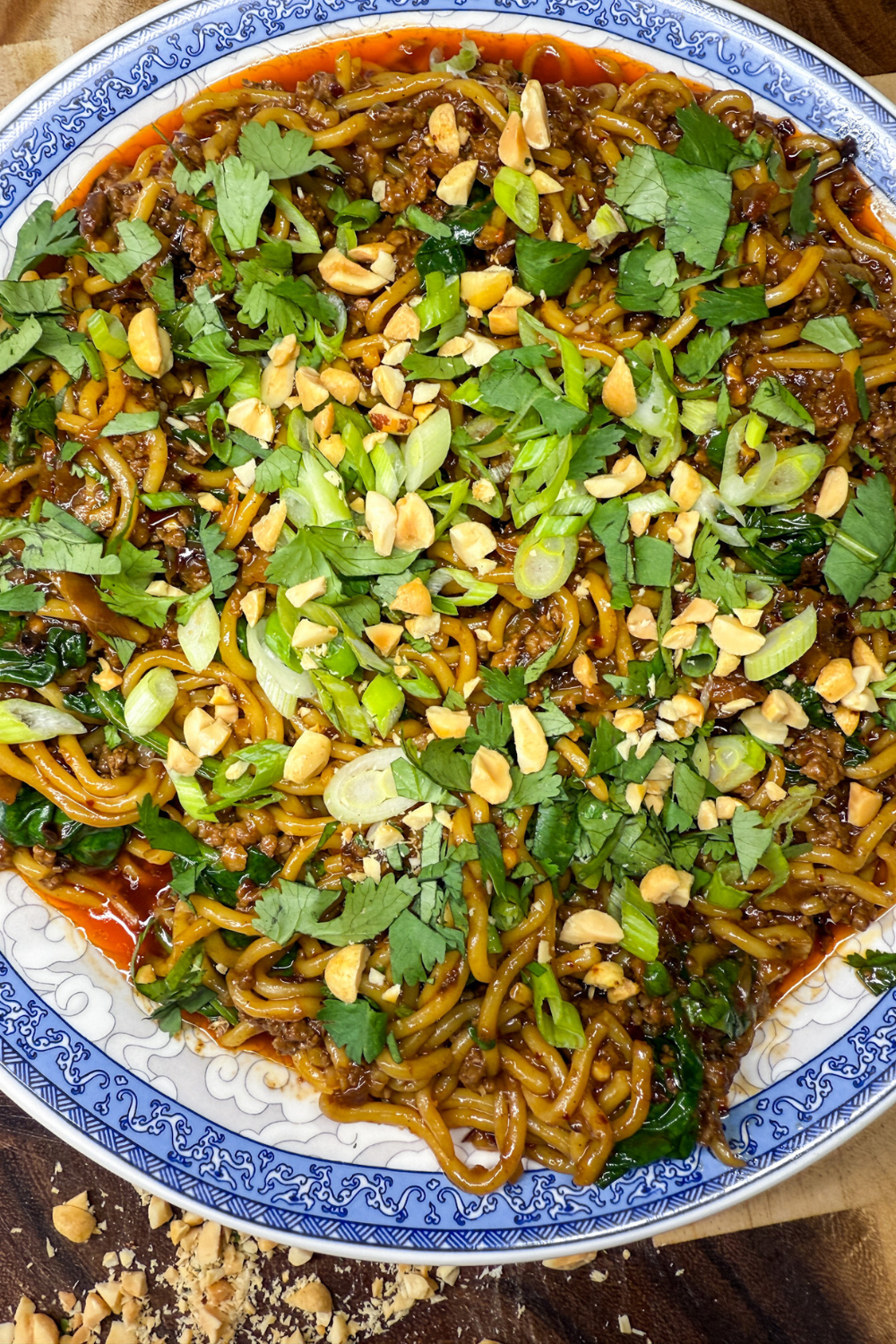 Family-style platter of spicy Dan Dan noodles topped with peanuts, scallions, and cilantro