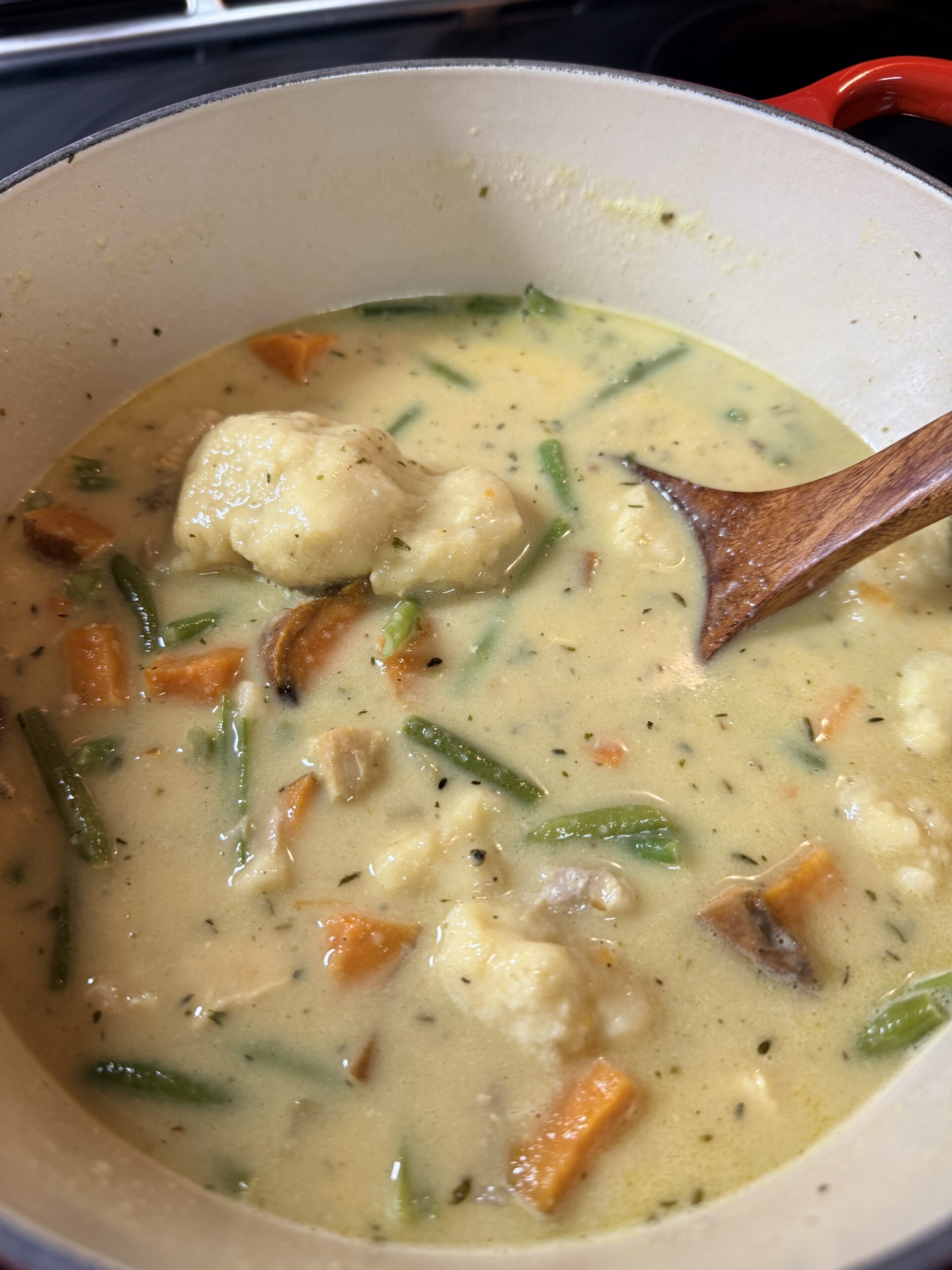 Chicken and dumplings soup cooking in Dutch oven with vegetables and creamy broth
