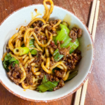 Spicy Dan Dan noodles with ground pork, bok choy, and chili crisp served in a bowl with chopsticks
