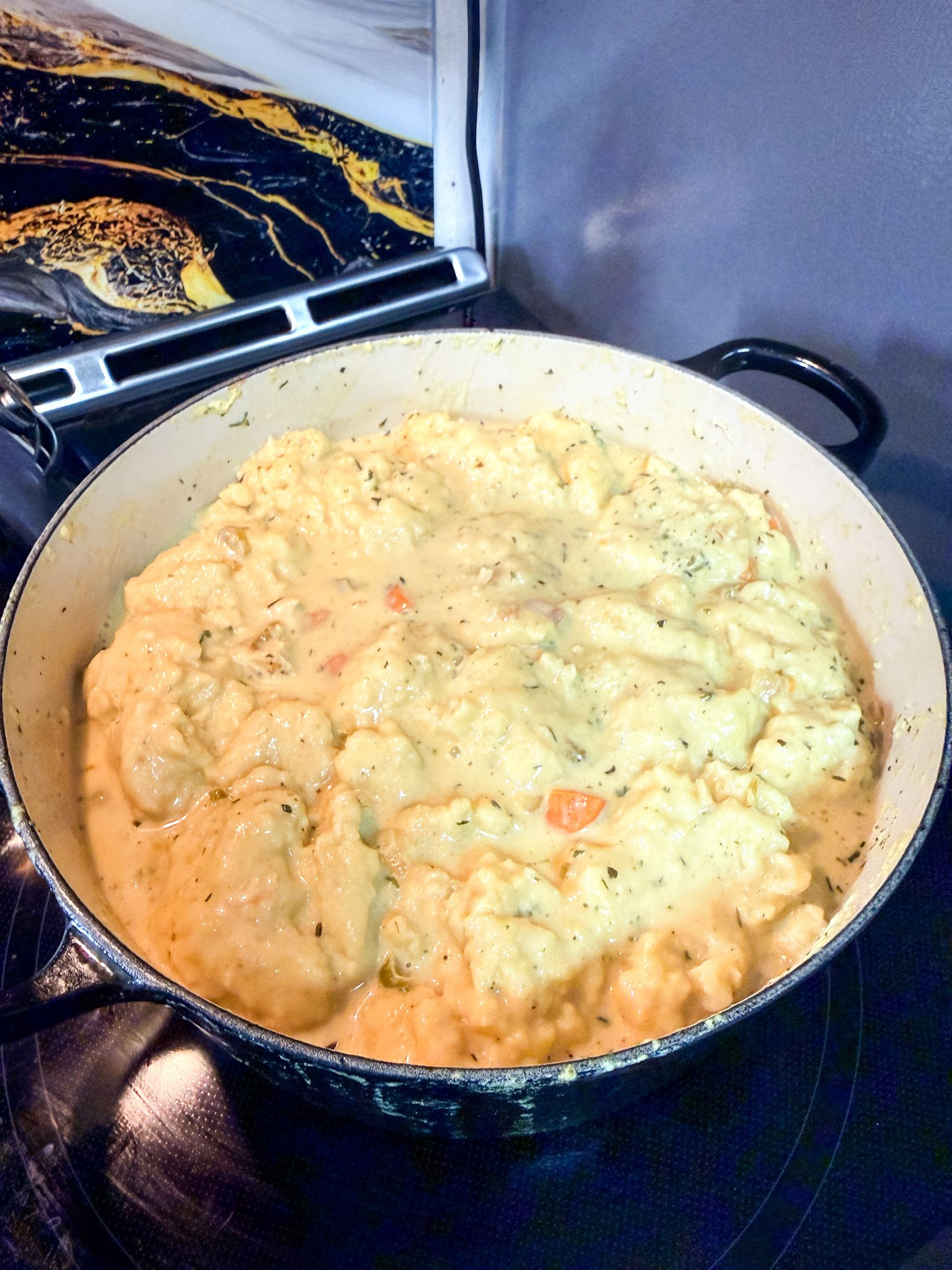 Homemade dumplings steaming on top of chicken and dumplings soup in pot