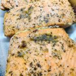 Fool-proof oven-baked salmon served on a plate with herbs and olive oil, showing tender flaky texture