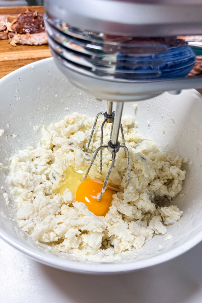 Adding eggs and cream to mashed potatoes for croquette mixture