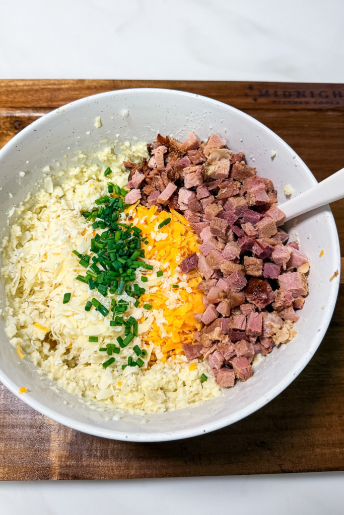 Adding chopped ham, shredded cheese, and chives to potato mixture