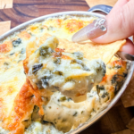 Creamy spinach artichoke dip scooped onto a tortilla chip showing melted cheese stretch.