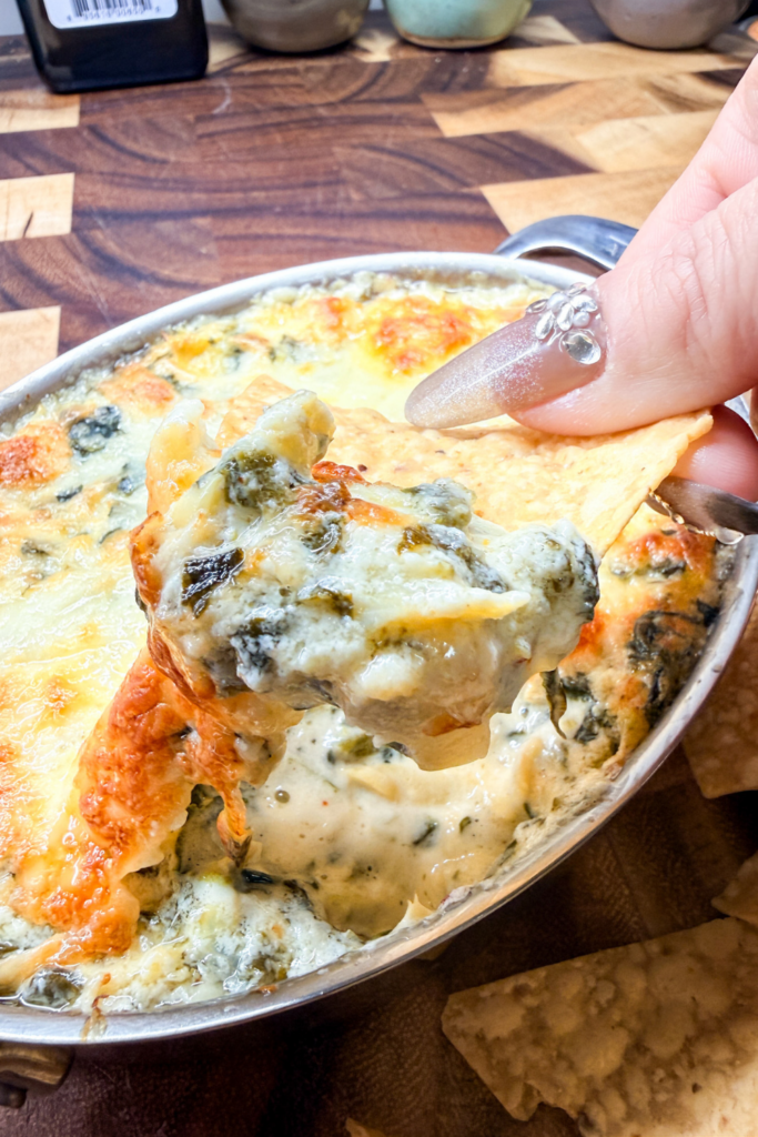 Creamy spinach artichoke dip scooped onto a tortilla chip showing melted cheese stretch.