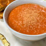 Creamy tomato basil soup in a white bowl topped with parmesan served with grilled cheese sandwiches
