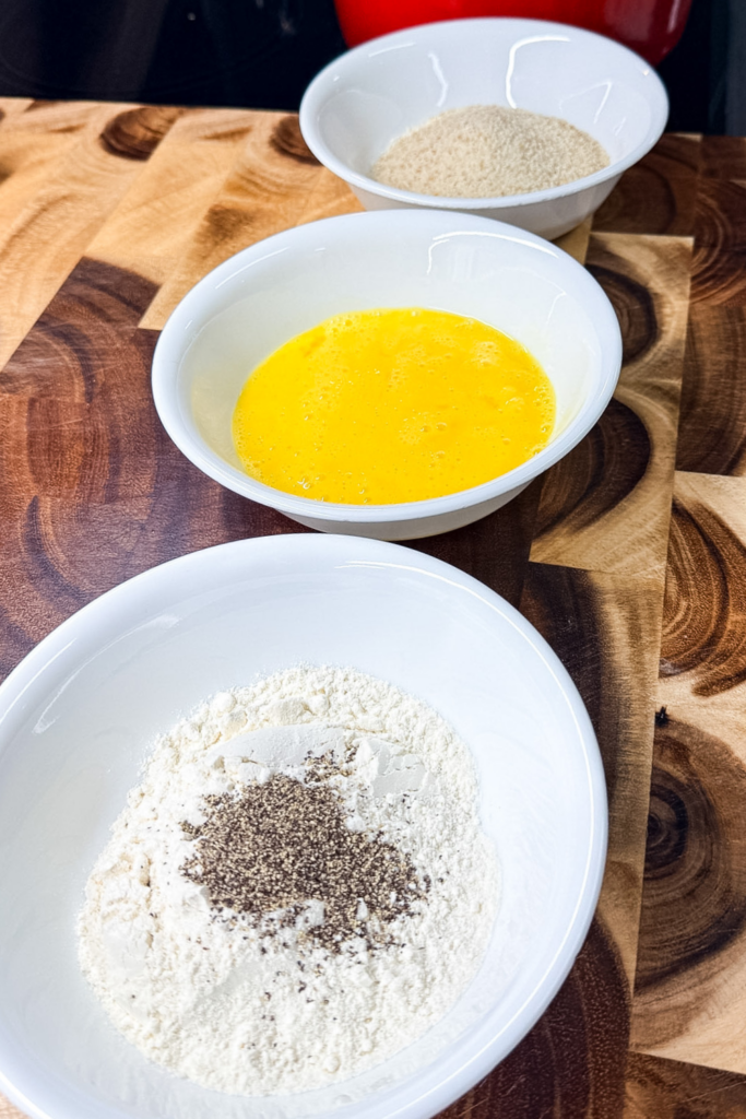 Breading station setup with flour, egg wash, and breadcrumbs for croquettes